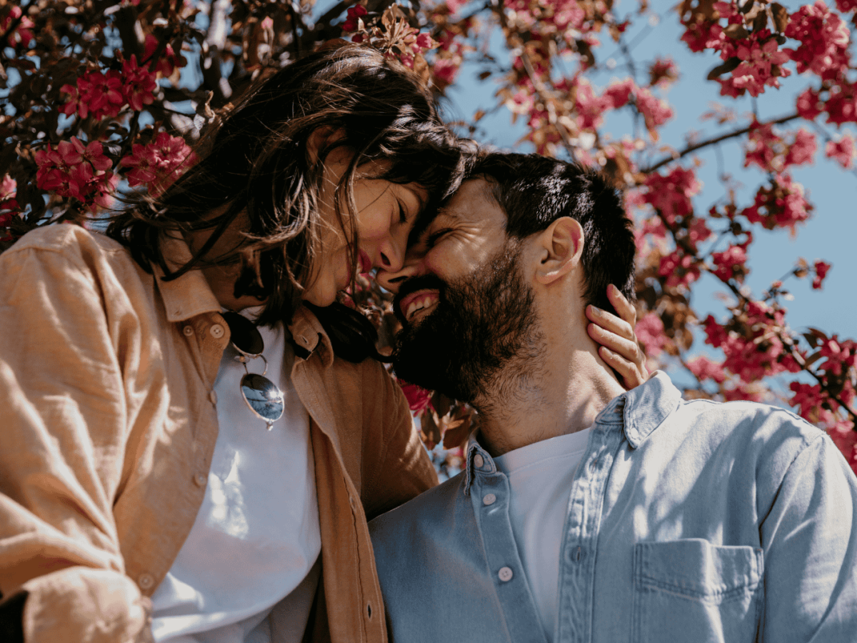 Frau und Mann Stirn an Stirn schauen sich innig in die Augen umgeben von Kirschbl&uuml;ten und blauem Himmel bei Sonnenschein