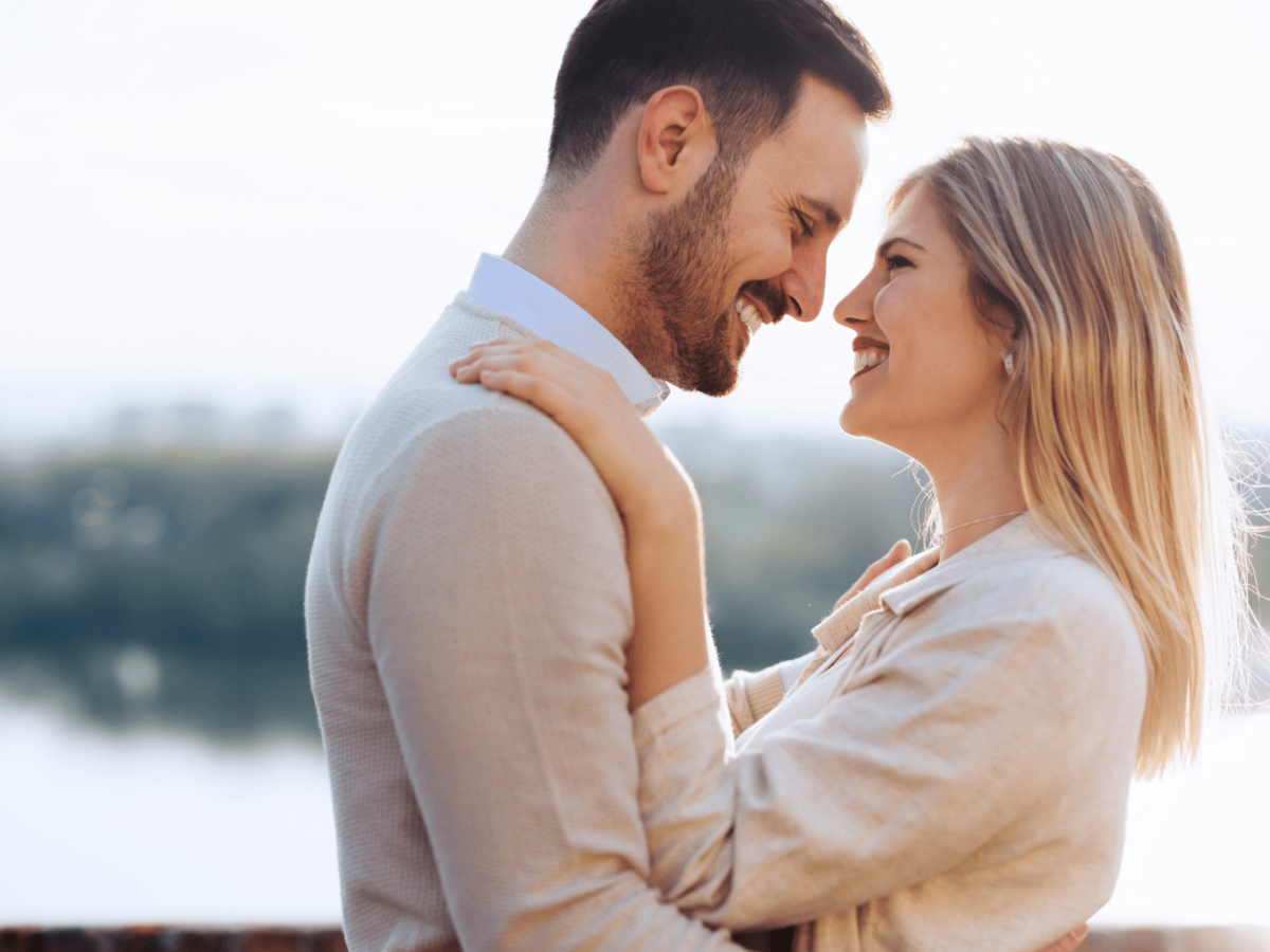 Frau und Mann stehen sich am Wasser gegen&uuml;ber und schauen sich l&auml;chelnd in die Augen