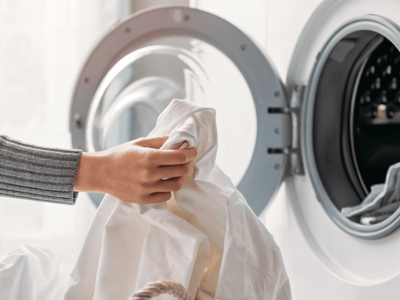 Person räumt weißes Kleidungsstück in die Waschmaschine