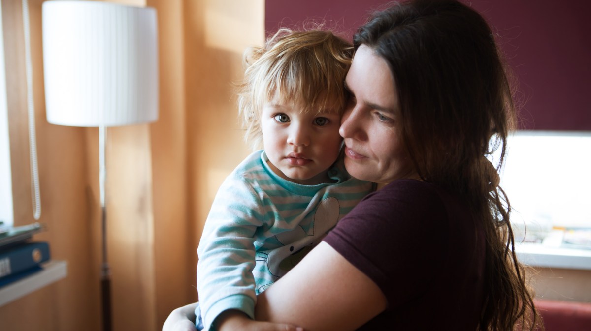 Mutter trägt trauriges Kind auf dem Arm.