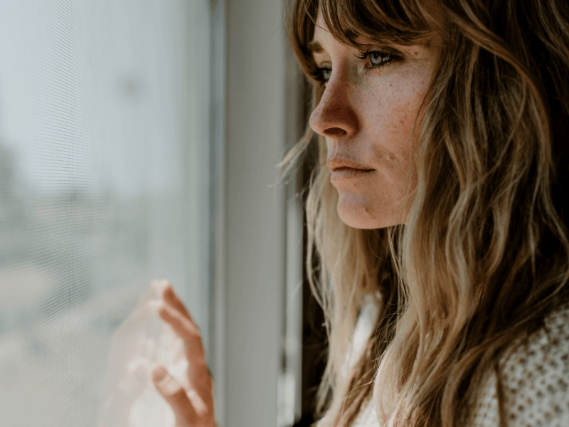 Junge Frau schaut traurig aus dem Fenster.