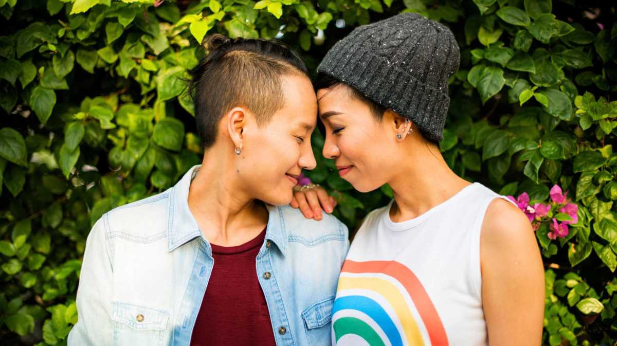 Junges, lesbisches Pärchen steht Stirn an Stirn zusammen und lächelt sich an.