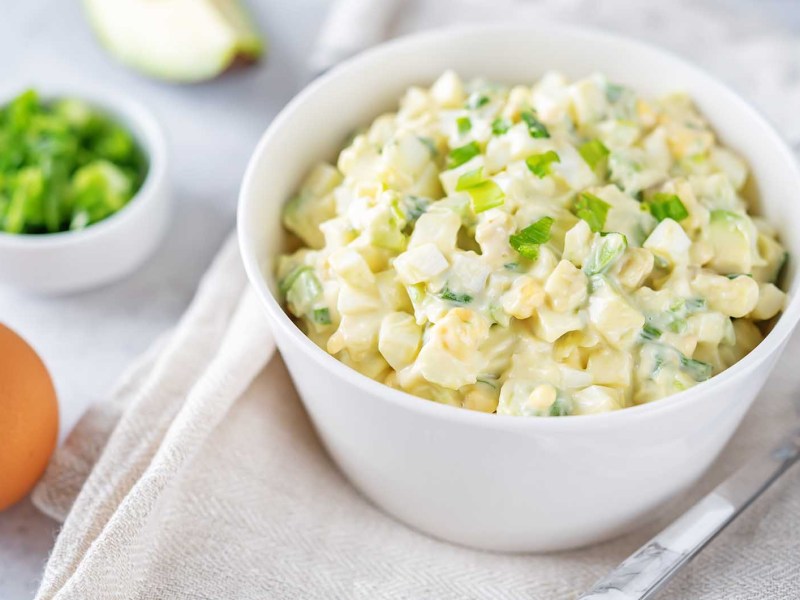 Eine Schüssel mit Eiersalat steht auf einem Tisch mit Tischdecke.
