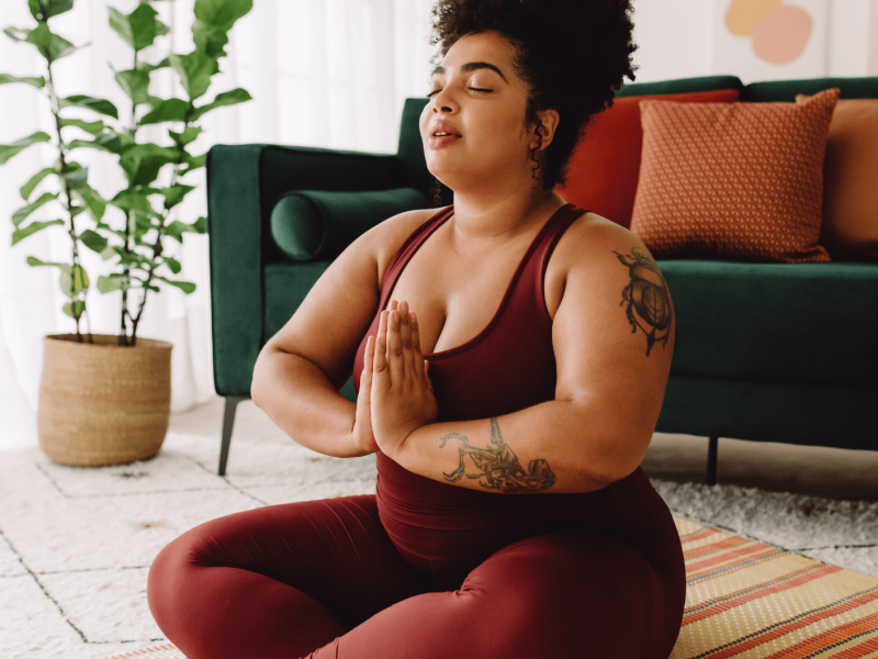 Kurvige Frau macht Yoga im Wohnzimmer.