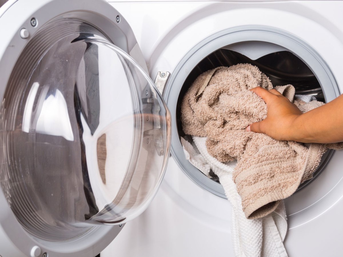 Hand gibt Handt&uuml;cher in Waschmaschine