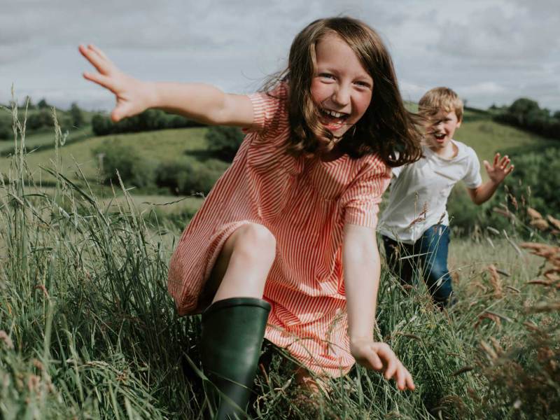 Zwei Kinder rennen im Sommer über ein Feld auf die Kamera zu.