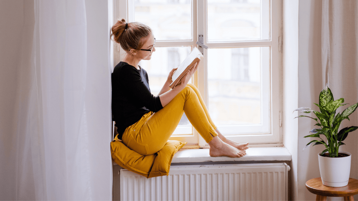 Frau sitzt auf Fensterbank und liest ein Buch.