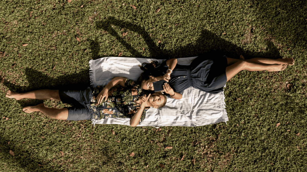 Mann und Frau liegen auf Wiese und legen mit einem PocketBook eReader.