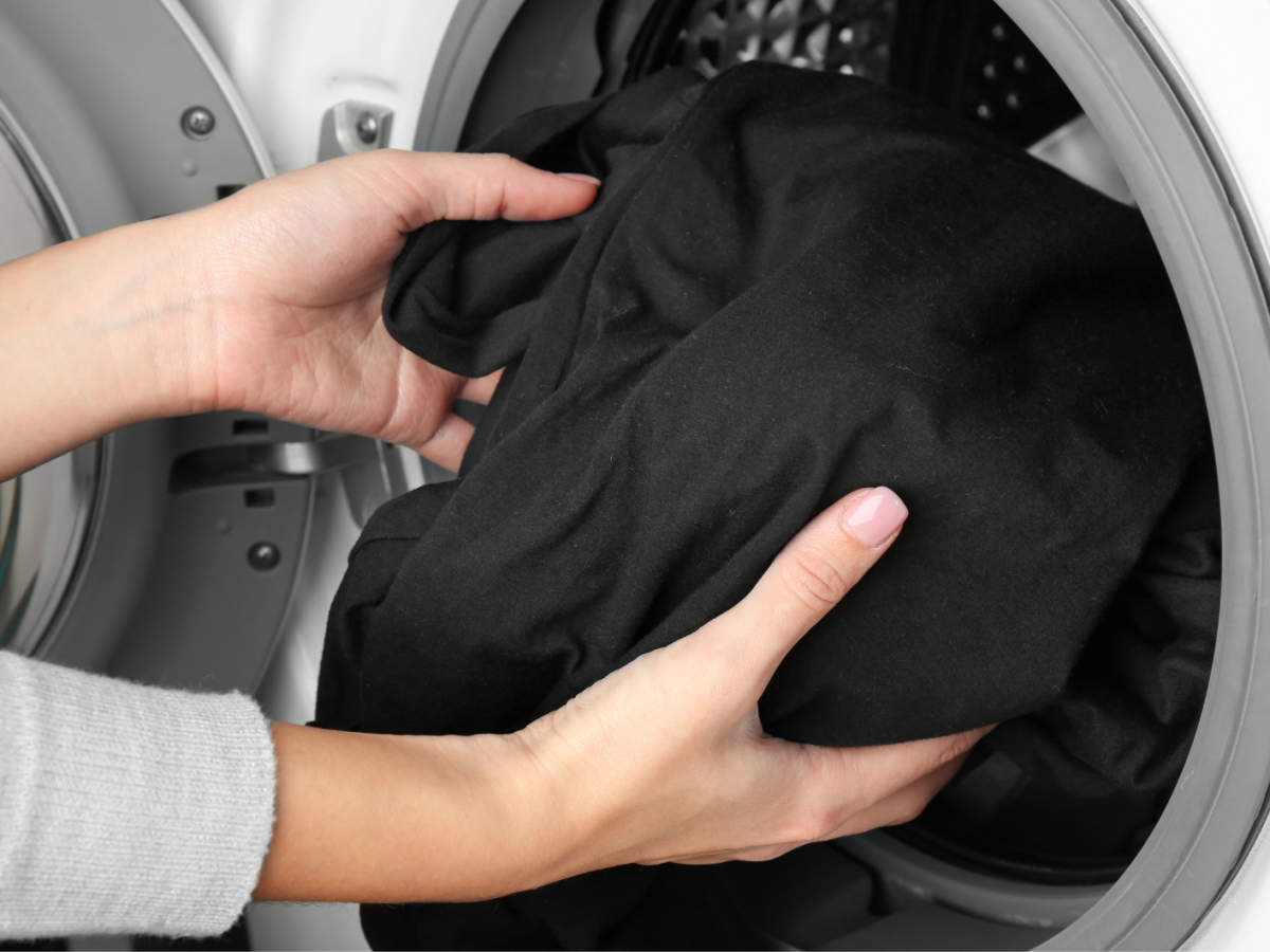 Frauenhände geben ein schwarzes Kleidungsstück in die Waschmaschine