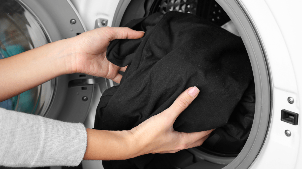 Frauenhände geben ein schwarzes Kleidungsstück in die Waschmaschine