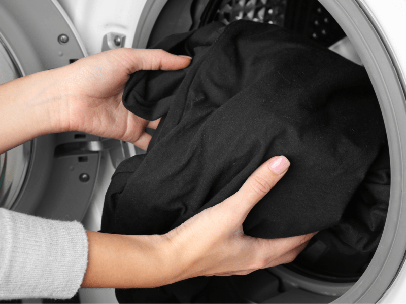 Frauenhände geben ein schwarzes Kleidungsstück in die Waschmaschine