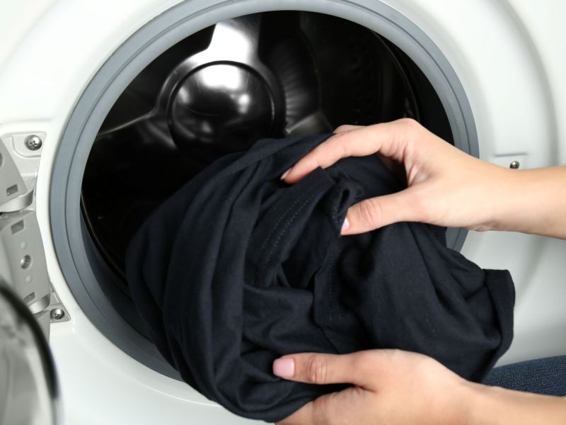 Hände nehmen schwarze Wäsche aus Waschmaschine