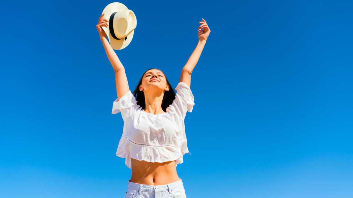 Frau streckt die Arme aus. Hinter ihr ist ein strahlend blauer HImmel.