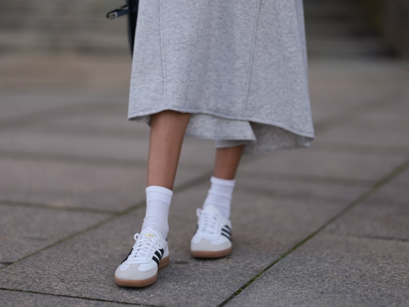 Nahaufnahme graues Wollstrickkleid, weiße Baumwollsocken und weiße Adidas-Leder-Samba-Sneaker.