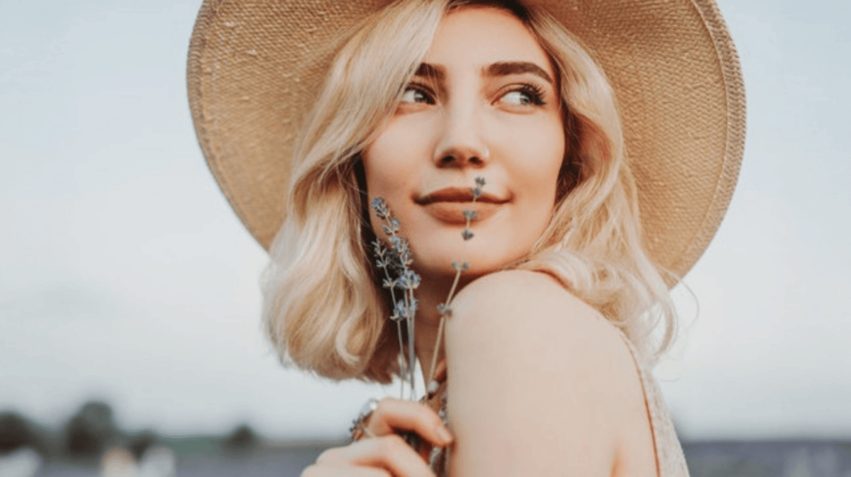 Junge Frau mit blonden Haaren hält Lavendel vor ihr Gesicht.