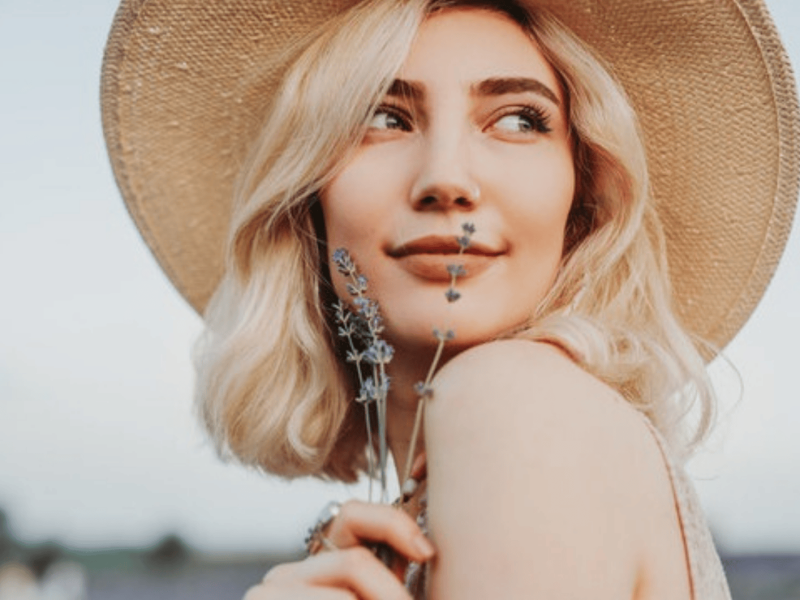 Junge Frau mit blonden Haaren hält Lavendel vor ihr Gesicht.