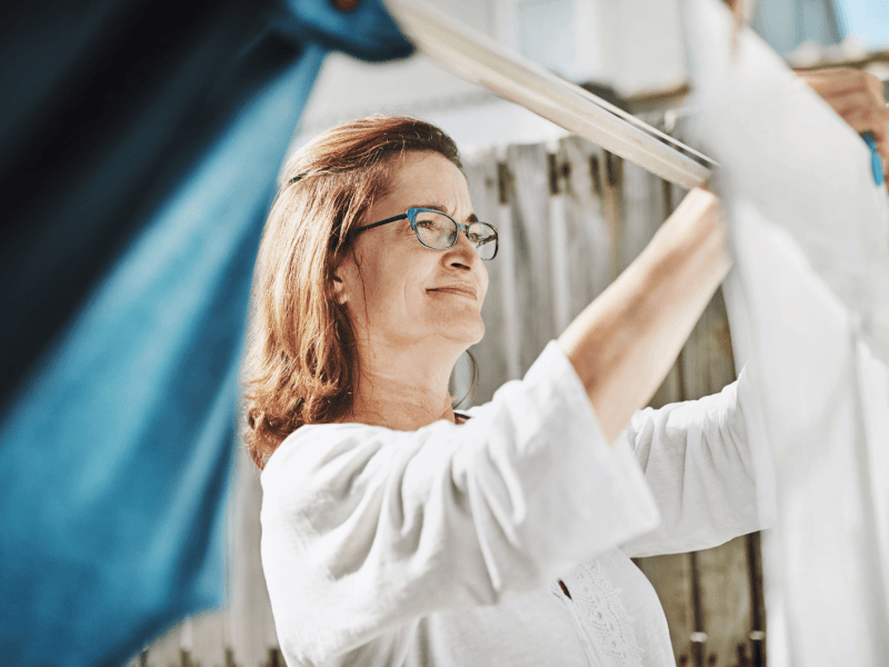 Frau hängt Wäsche auf Leine im Garten auf.