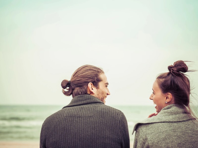 Paar sitzt gemeinsam am Meer und schaut sich an