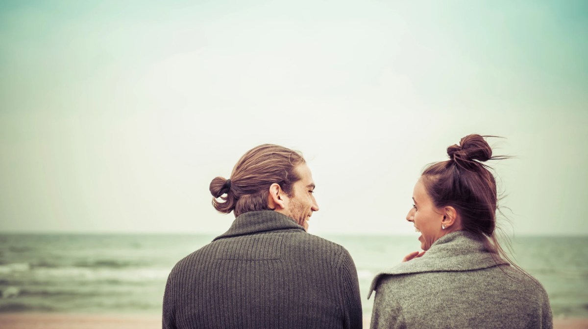 Paar sitzt gemeinsam am Meer und schaut sich an