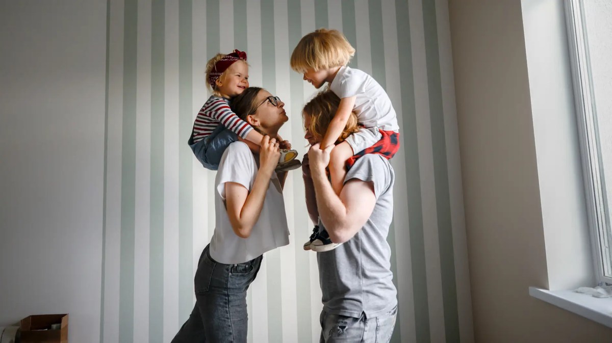 Mutter und Vater mit je einem Kind auf den Schultern.