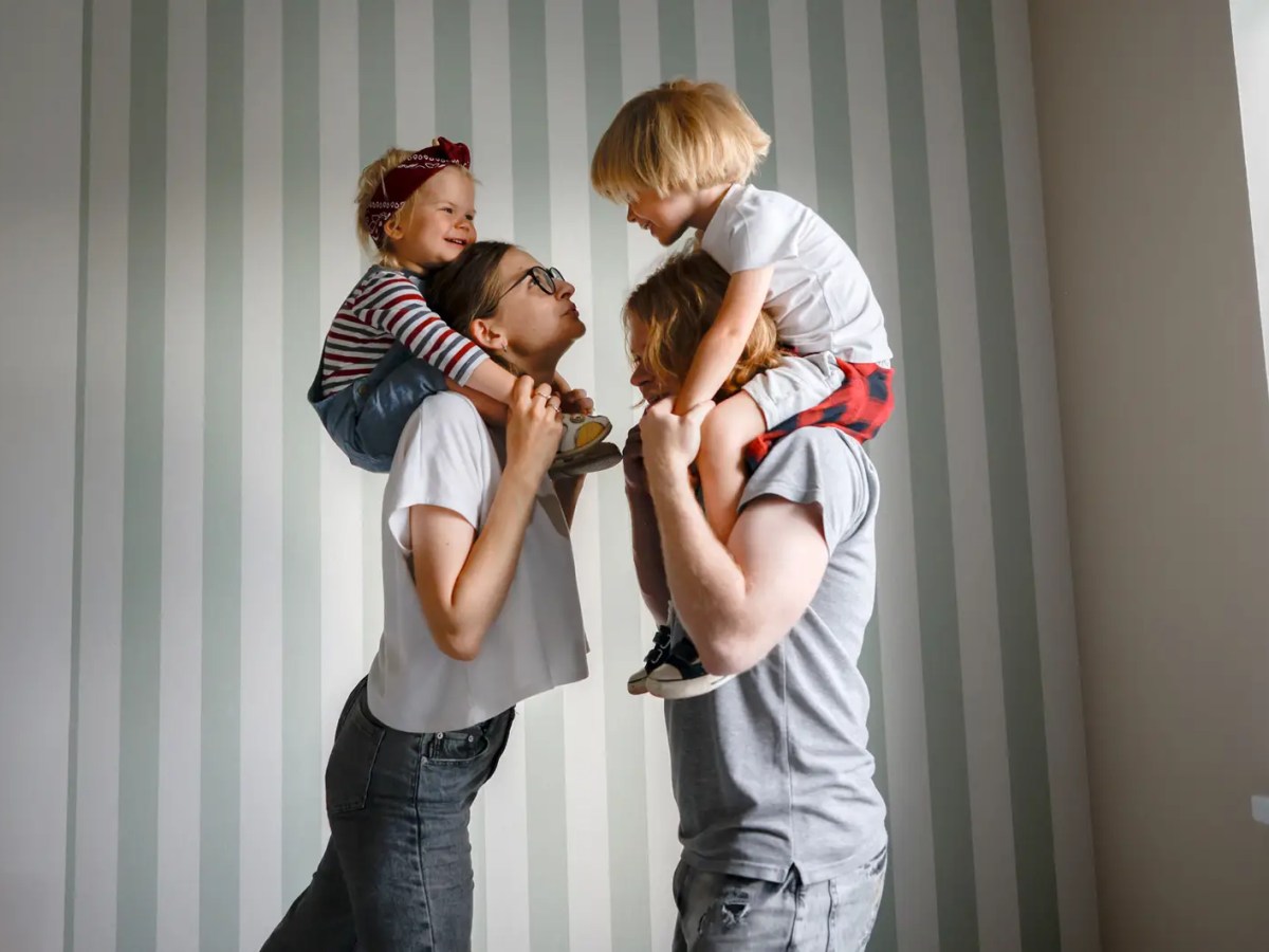 Mutter und Vater mit je einem Kind auf den Schultern.