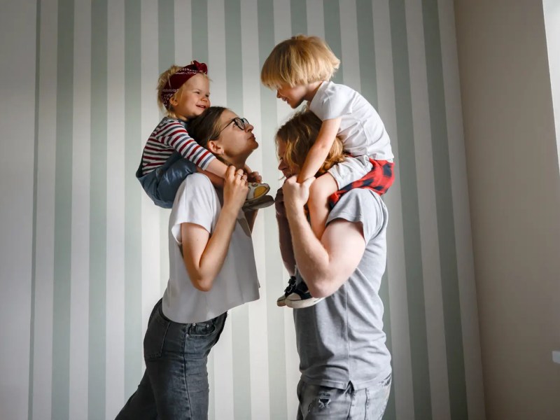 Mutter und Vater mit je einem Kind auf den Schultern.