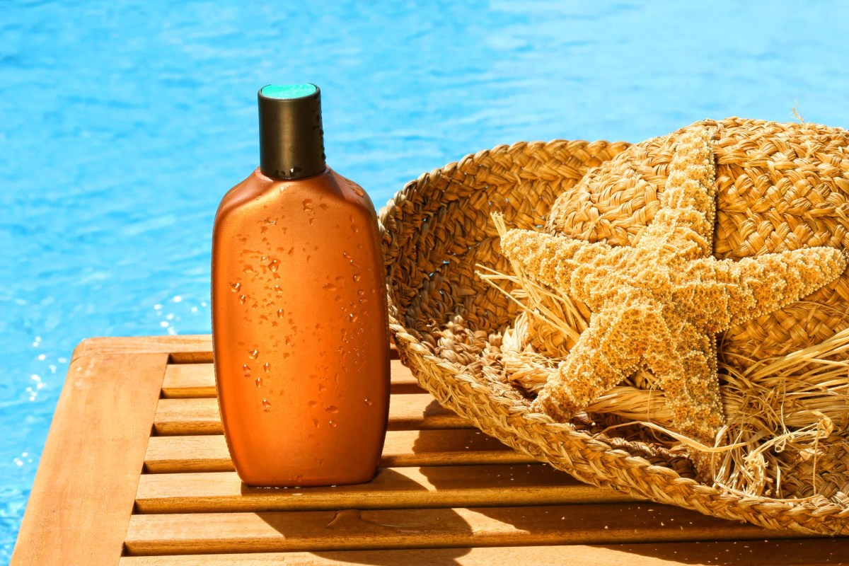 Eine Tube Sonnencreme vor einem blauen Pool und neben einem Sonnenhut.