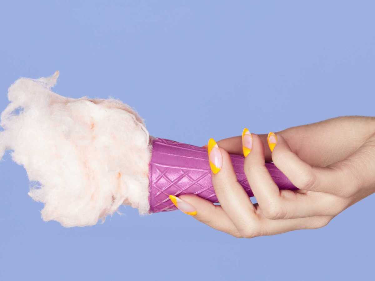 Hand mit gelb lackierten Fingern&auml;geln h&auml;lt ein Eis fest