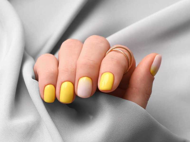 Gelb lackierte Fingernägel vor einem grauen Seidentuch
