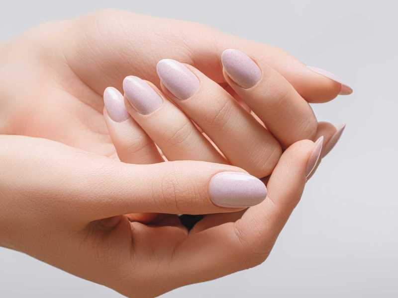 Eine Hand mit beige lackierten Fingernägeln liegt in der anderen Hand