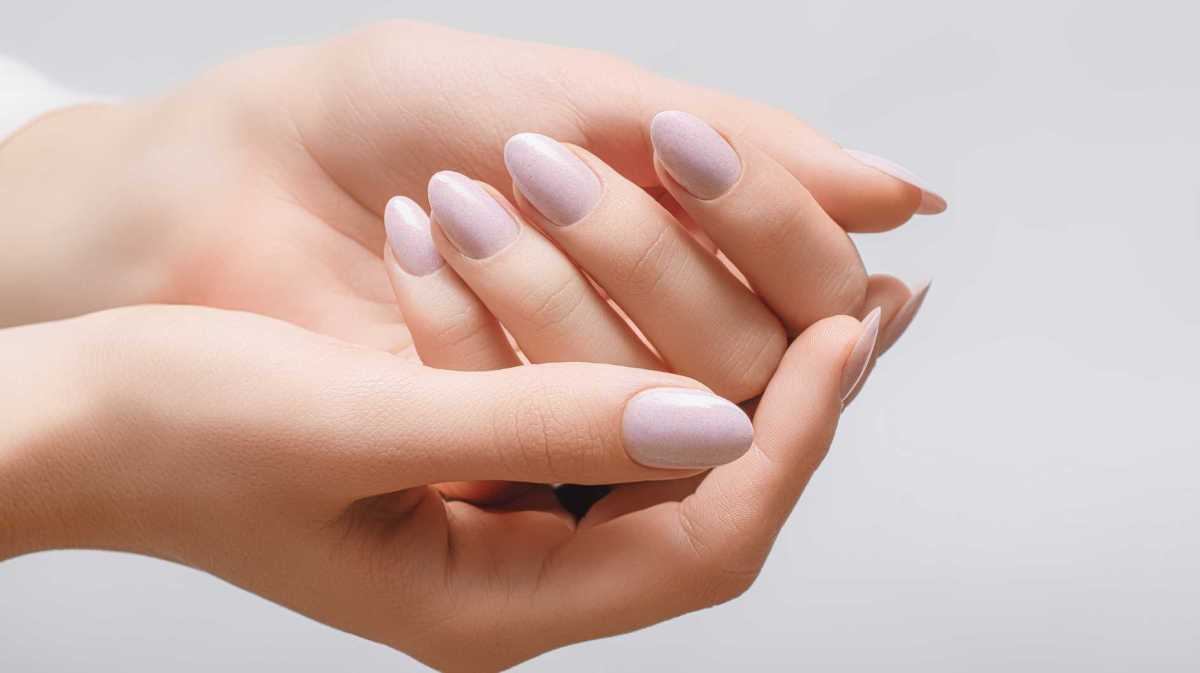 Eine Hand mit beige lackierten Fingernägeln liegt in der anderen Hand