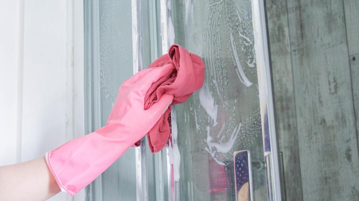 Frau reinigt eine Duschtüre mit einem Lappen.