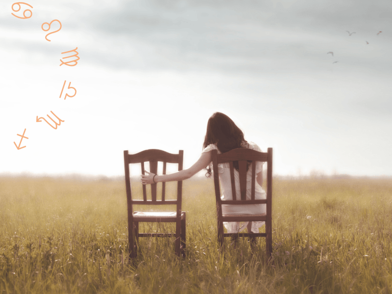 Frau sitzt auf dem Feld auf einem Stuhl und hält Hand auf leeren Stuhl neben ihr