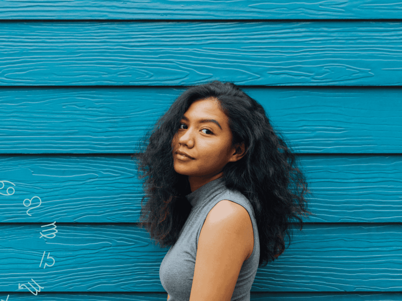 Frau mit dunklen Locken steht vor blau-gebretterter Wand