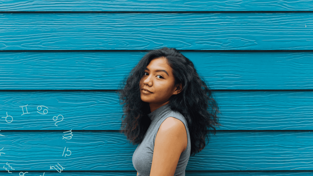 Frau mit dunklen Locken steht vor blau-gebretterter Wand