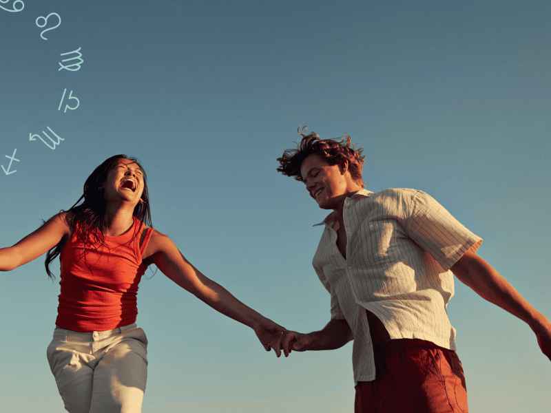 Frau und Mann halten sich an der Hand und lachen zusammen vor blauem Himmel