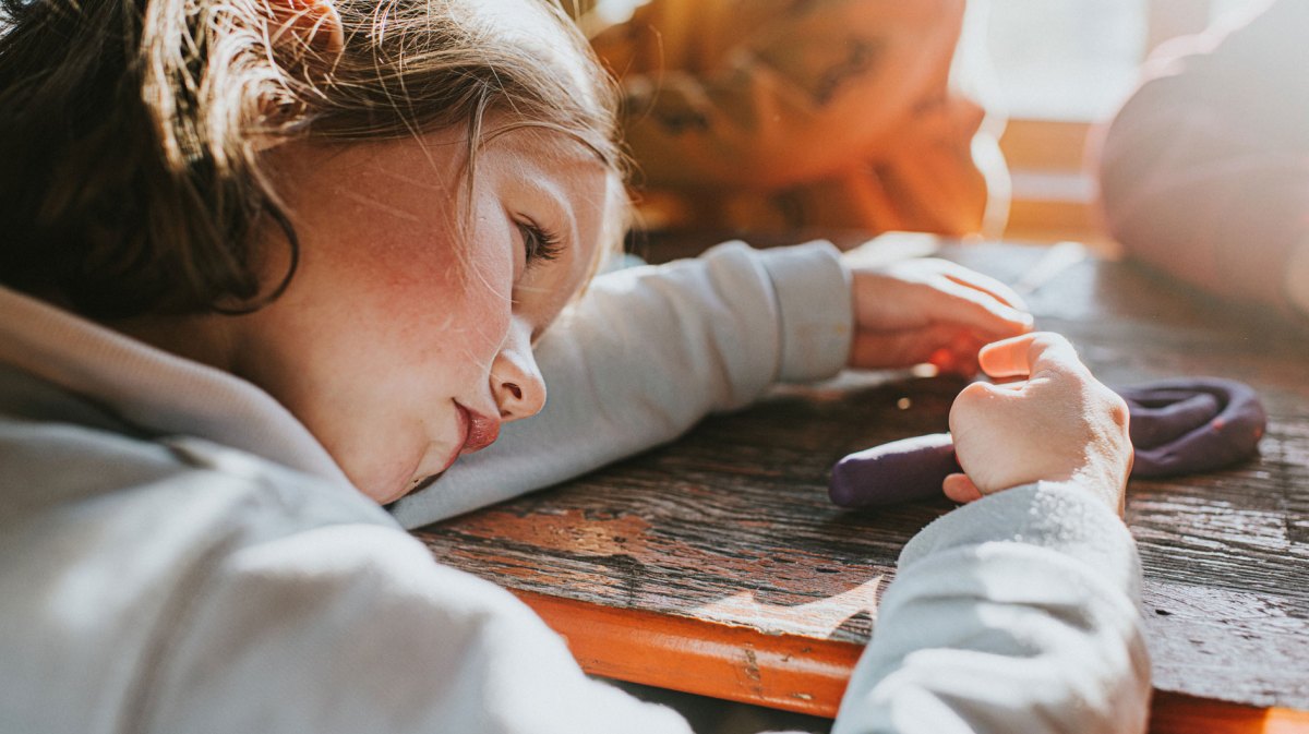 Mädchen legt ihren Kopf auf ihrem Arm auf dem Schreibtisch ab, während es knetet.