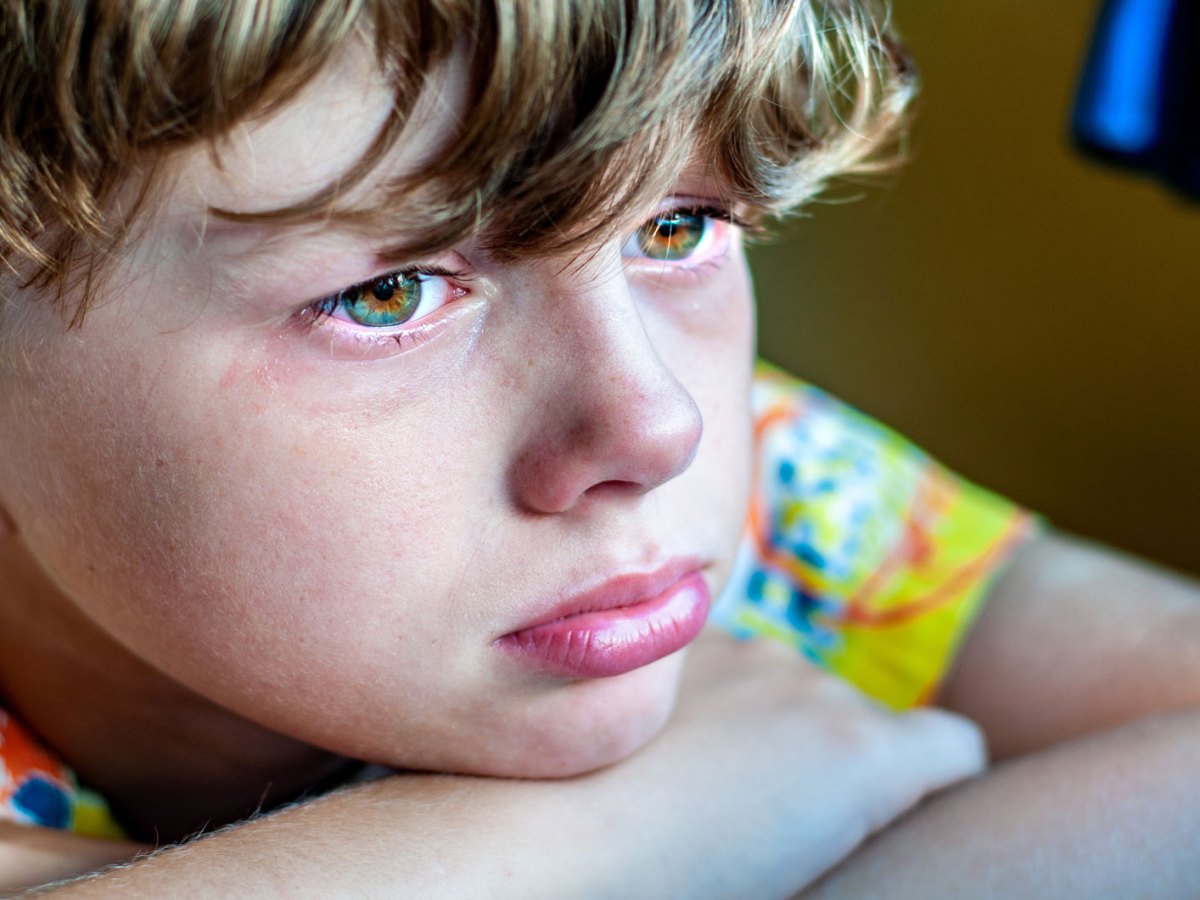 Profil eines traurigen Jungen, der den Kopf auf den auf einem Tisch liegenden verschr&auml;nkten Armen abgelegt hat.