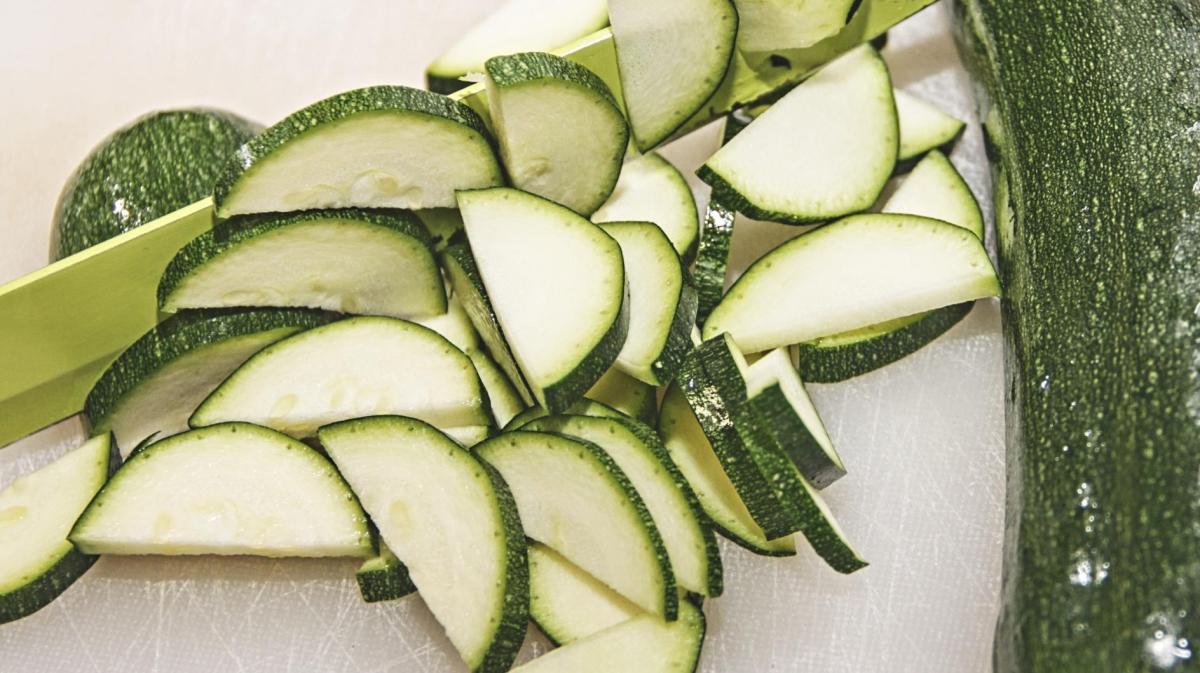 Geschnittene rohe Zucchini liegt auf einem Brett mit einem Messer.