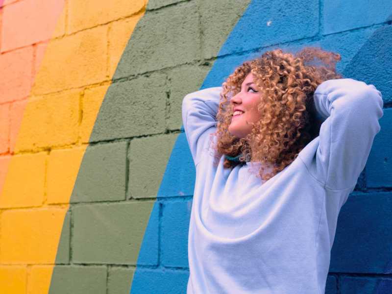 Junge Frau lehnt sich an eine bunte Wand.