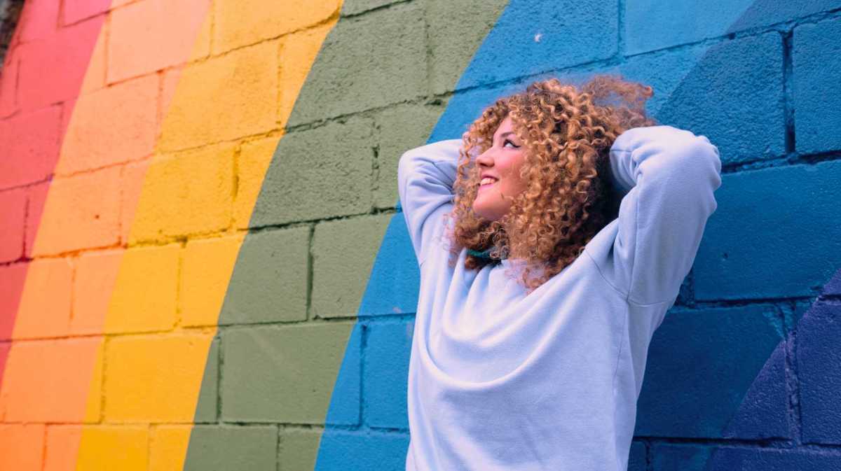 Junge Frau lehnt sich an eine bunte Wand.