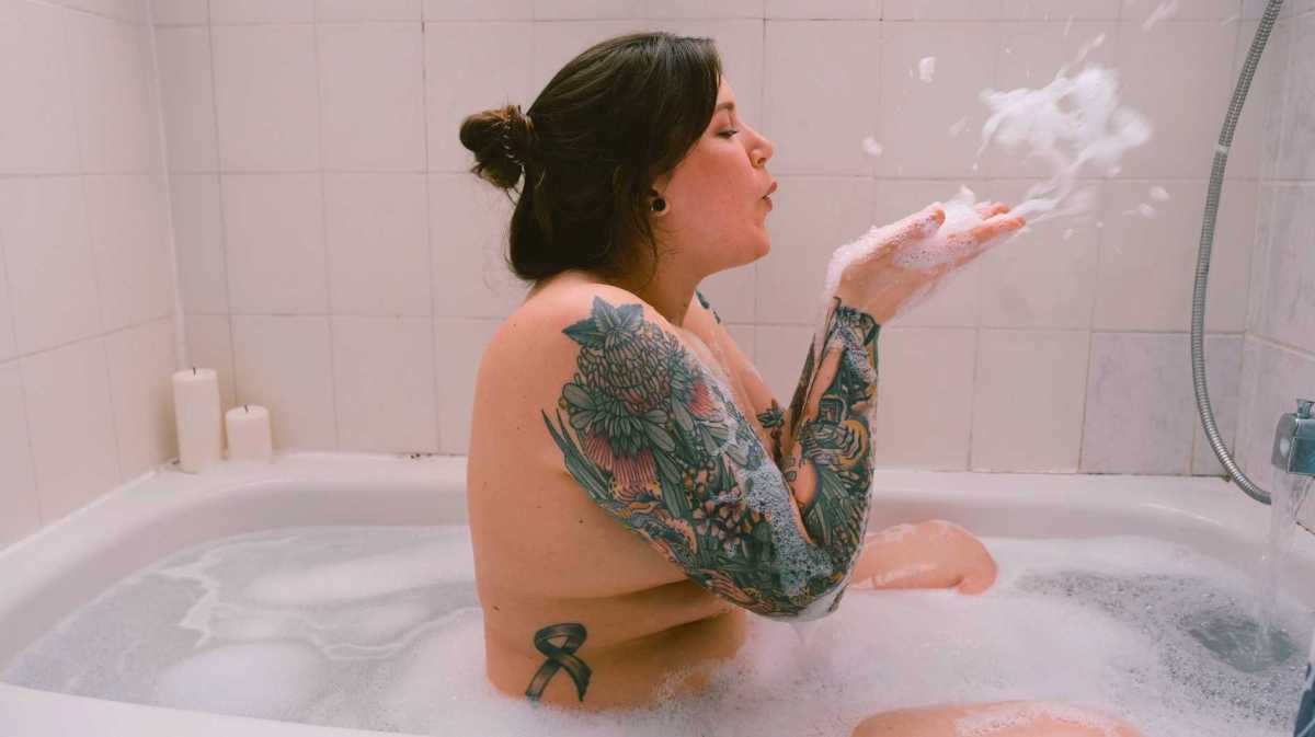 Junge Frau sitzt in der Badewanne voller Schaum.