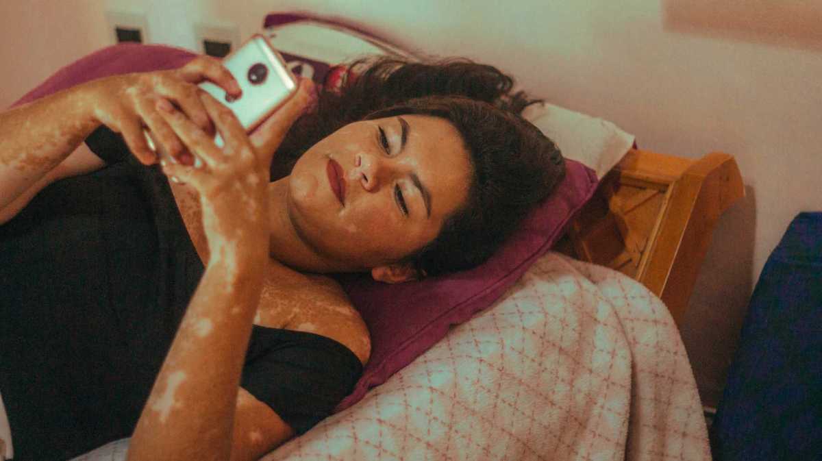 Junge Frau liegt auf ihrem Bett und benutzt ihr Handy.