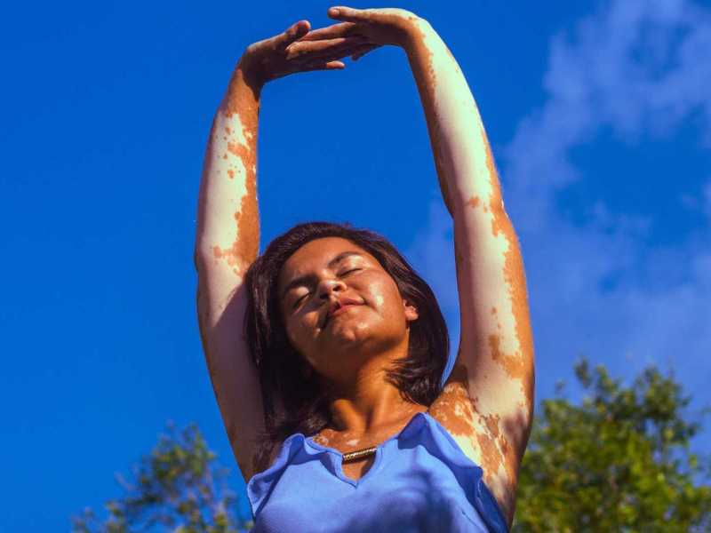 Frau mit ausgestreckten Armen und blauem Himmel im Hintergrund.