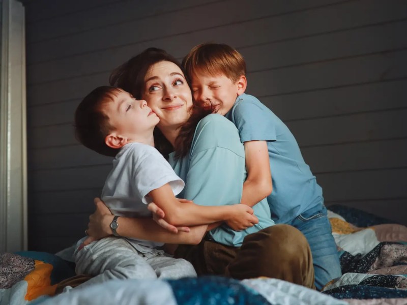 Mutter im Bett, wird von ihren beiden Söhnen am Morgen herlzlich geweckt.