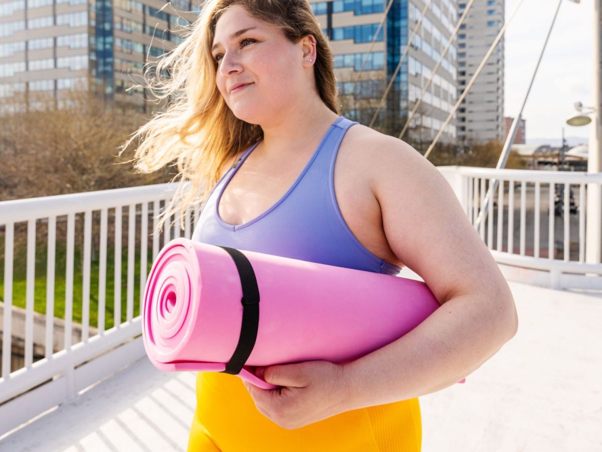 Frau mit Sportkleidung und pinker Sportmatte unter dem Arm drau&szlig;en