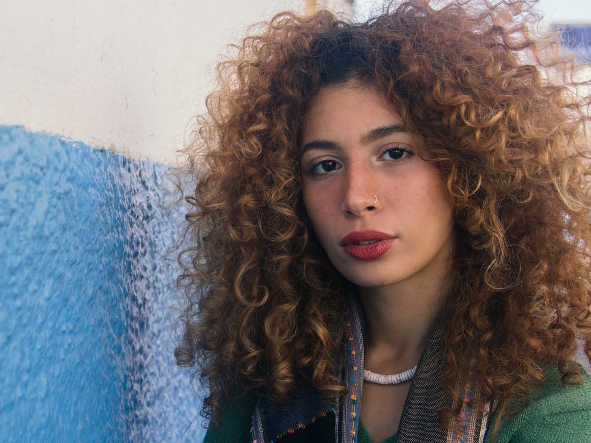 Frau mit Locken steht in einer Straße und schaut in die Kamera.