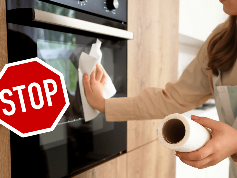 Frau wischt über Ofen mit Küchenrolle.