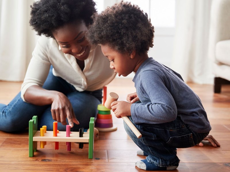 Mutter und Sohn sitzen auf dem Fußboden und spielen ein Hammer-Spiel.