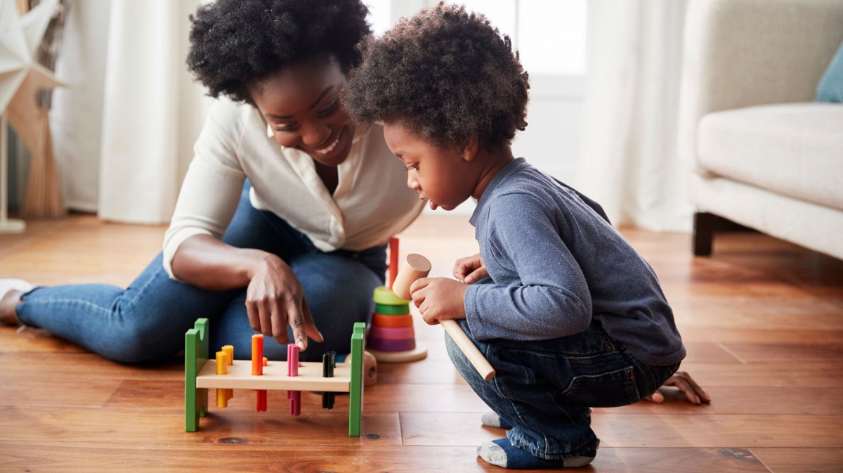 Mutter und Sohn sitzen auf dem Fußboden und spielen ein Hammer-Spiel.